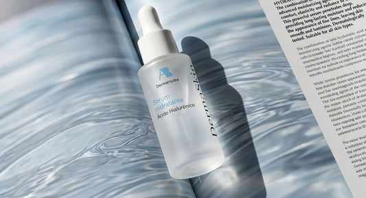 Sérum Hidratante con ácido hialurónico de DermaSkin sobre un libro abierto con reflejos de agua, representando la hidratación de la piel en verano.